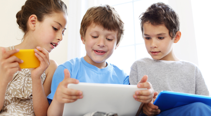 Ein Mädchen mit einem Smartphone und zwei Jungen mit Tablets